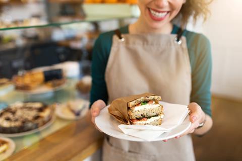 A smiley woman in a beige apron serving a sandwich on a plate