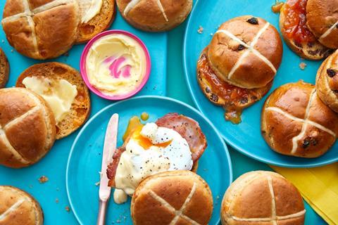 Hot cross buns on blue plates, one with eggs and bacon on top