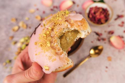 A pistachio & rose doughnut with a bite taken out of it and pistachio filling oozing out