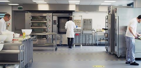 Three men in a test bakery with ovens, mixers and provers