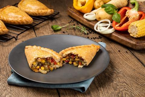 A Vegetable Pasty on a black plate with a selection of vegetables in the background