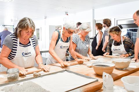 Women in aprons rolling dough on a wooden surface