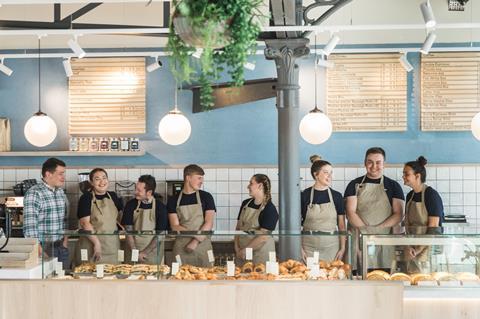 A group of Cornish Bakery staff in navy t-shirts and beige aprons behind a counter of baked goods