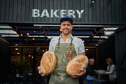 Tim Goodwin in a denim cap holding two loaves of sourdough outside his bakery