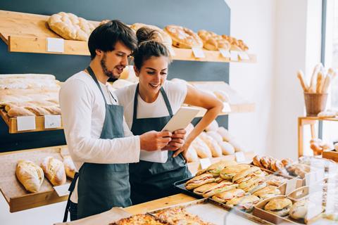 Two bakers in blue aprons looking at a tablet