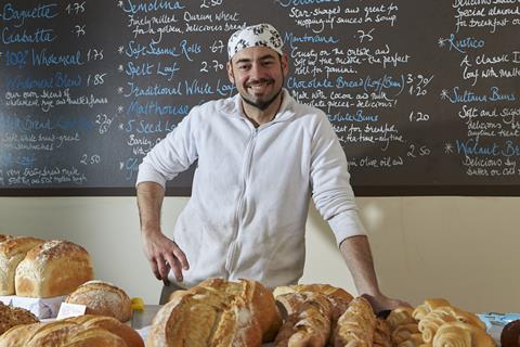 Denis Casella, a baker in front of loaves of bread with a handwritten board behind him