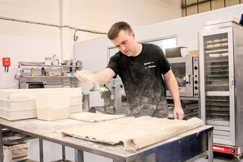 Jordan Skeet, a baker at Bread Source, sprinkling flour onto pastry