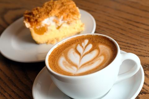 A latte in a white cup with a cake in the background