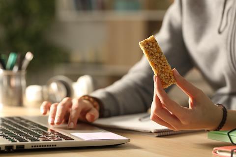 A granola bar held by a person operating a laptop