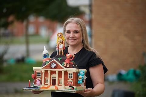 Kerry Smith holding her nostalgia themed cake with characters from 1980s TV shows and movies on