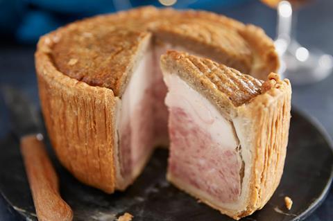 A large pork pie with a slice taken out to reveal a layer of chicken, stuffing and pork