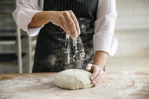 A woman sprinkling flour on dough