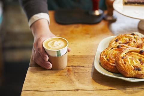 A barista handing over a coffee next to pain au raisin
