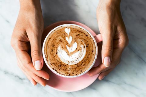 A white person holding a pink cup with a coffee in it