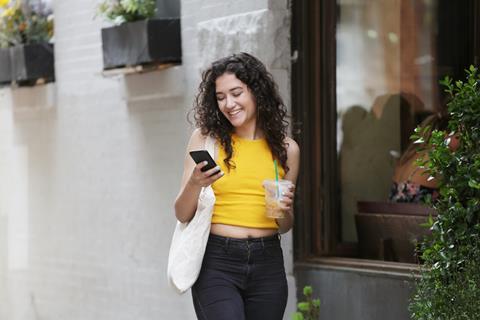 Millennial smiles while holding a cell phone and ice coffee
