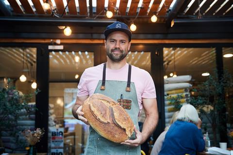 Tim Goodwin, a baker with a beard and baseball cap, holding a loaf of sourdough
