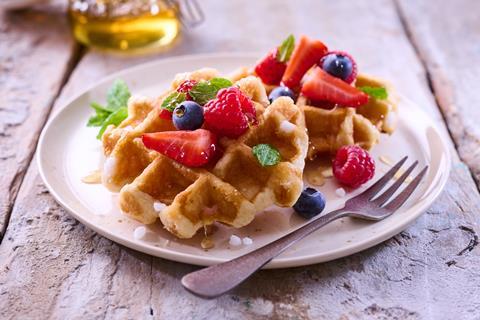 A lifestyle image of two waffles topped with fresh berries and mint leaves