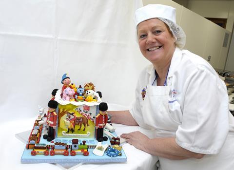 A woman in a baker's jacket and hair net next to a celebration cake