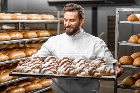 A baker with a beard holding a tray of fresh croissants