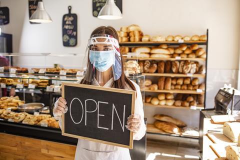 Woman in mask holding open sign in bakery