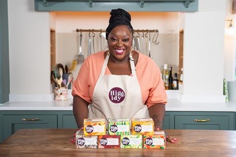 Comedian Judi Love stood wearing a Higgidy branded apron in front of a counter with pies on it