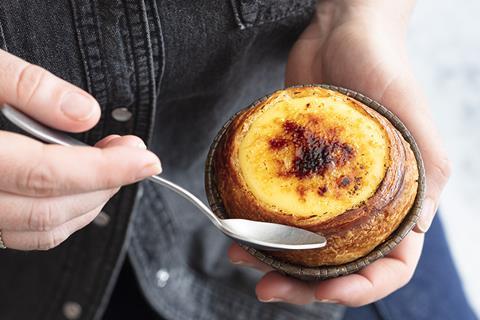 A person eating creme brulee from the top of a brioche roll