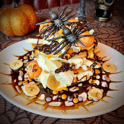 A stack of Halloween pancakes with cream, banana, chocolate sauce and fake spiders