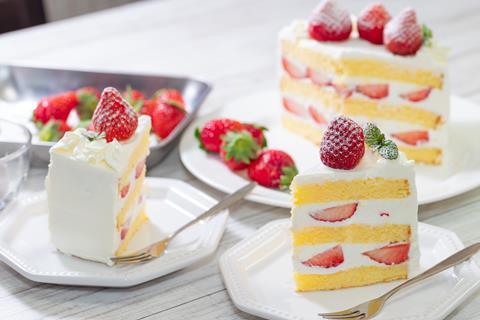 A sliced up vanilla cake with lashings of cream and strawberries