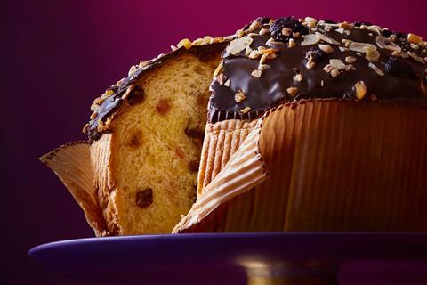 A panettone with a slice taken out of it, with chocolate, nuts and dried fruit on top