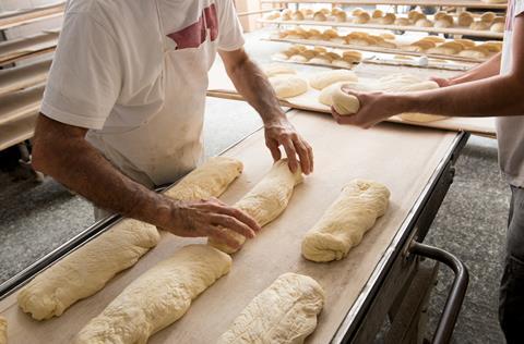 Bread dough being shaped by two male bakers