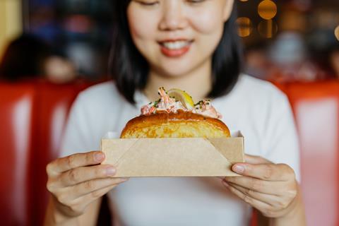 A woman holding a lobster roll in a brioche bun, topped with chives and lemon