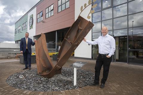 Mandy Jones - Jones Village Bakery CEO Simon Thorpe (right) stands with Cllr Nigel Williams by the  twisted metal girder placed in front of the company's headquarters in Wrexham as a reminder of the 2019 fire