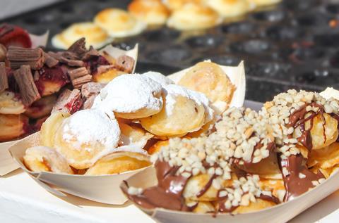 Mini Dutch pancakes smothered with icing sugar, chocolate, and nuts