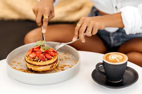 A young woman in denim shorts and white top eating pancakes