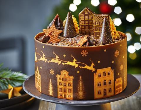 A chocolate cake with chocolate collar and edible tree and house decorations on top