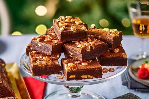 A pile of square brownies with gold lustred hazelnuts on top