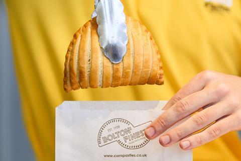 A pair of metal tongs help place a Carrs pasty in a paper bag for takeaway.