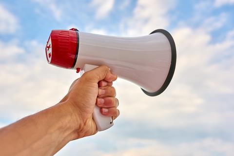 A megaphone being held by a white person's hand against a blue sky
