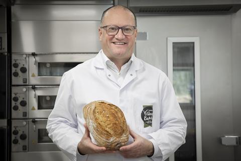 A man in a white baker's jacket holding a loaf of sourdough