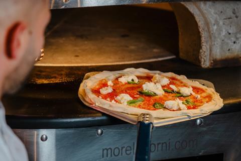 Chef Marco Greco puts a freshly prepared pizza into an oven.