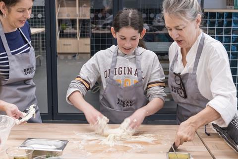 A girl is guided in  dough making by Bread Ahead team members at its baking school in Borough Market, London  2100x1400