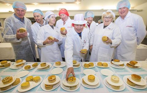 People in white coats and butchers' hats judging a selection of pies