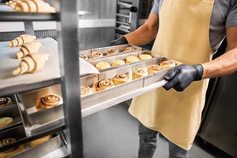 Baker with gloves on holding cinnamon bun tray