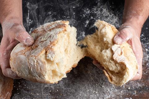 A white man breaking a warm sourdough loaf