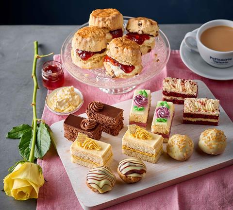 A pink tablecloth with jam and cream-filled scones, cake slices and a cup of tea