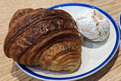 A croissant and an almond cookie on a white plate.