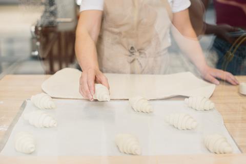 A woman placing raw croissant dough onto a baking tray