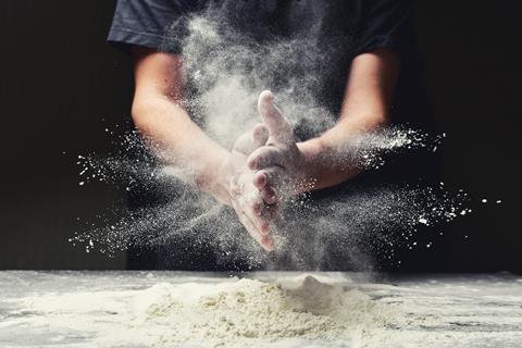 Baker making cloud of flour dust with hands while kneading dough