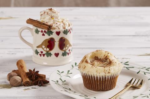 A gingerbread cupcake next to an inviting gingerbread latte topped with whipped cream and a cinnamon stick