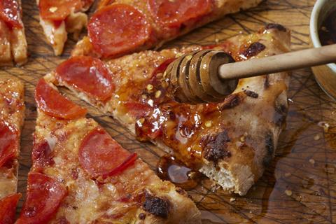 Hot honey being drizzled on pepperoni pizza